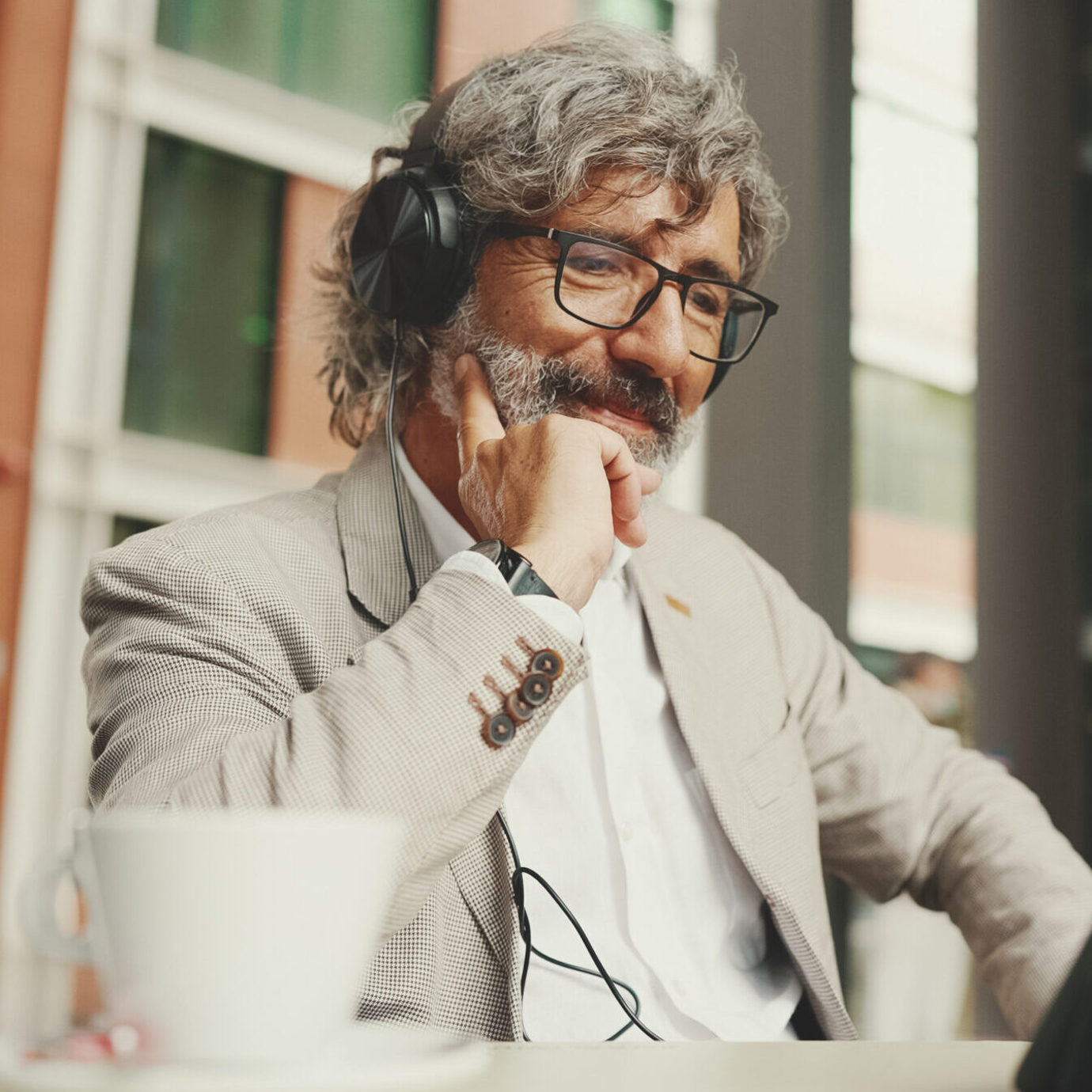 Senior businessman wearing glasses and smiling while working on a laptop in a modern office.