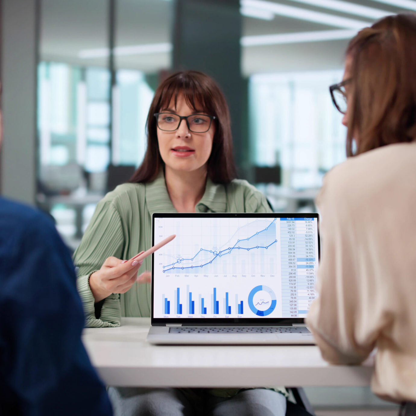 Financial adviser presenting charts and financial data on a laptop during a meeting with two colleagues.