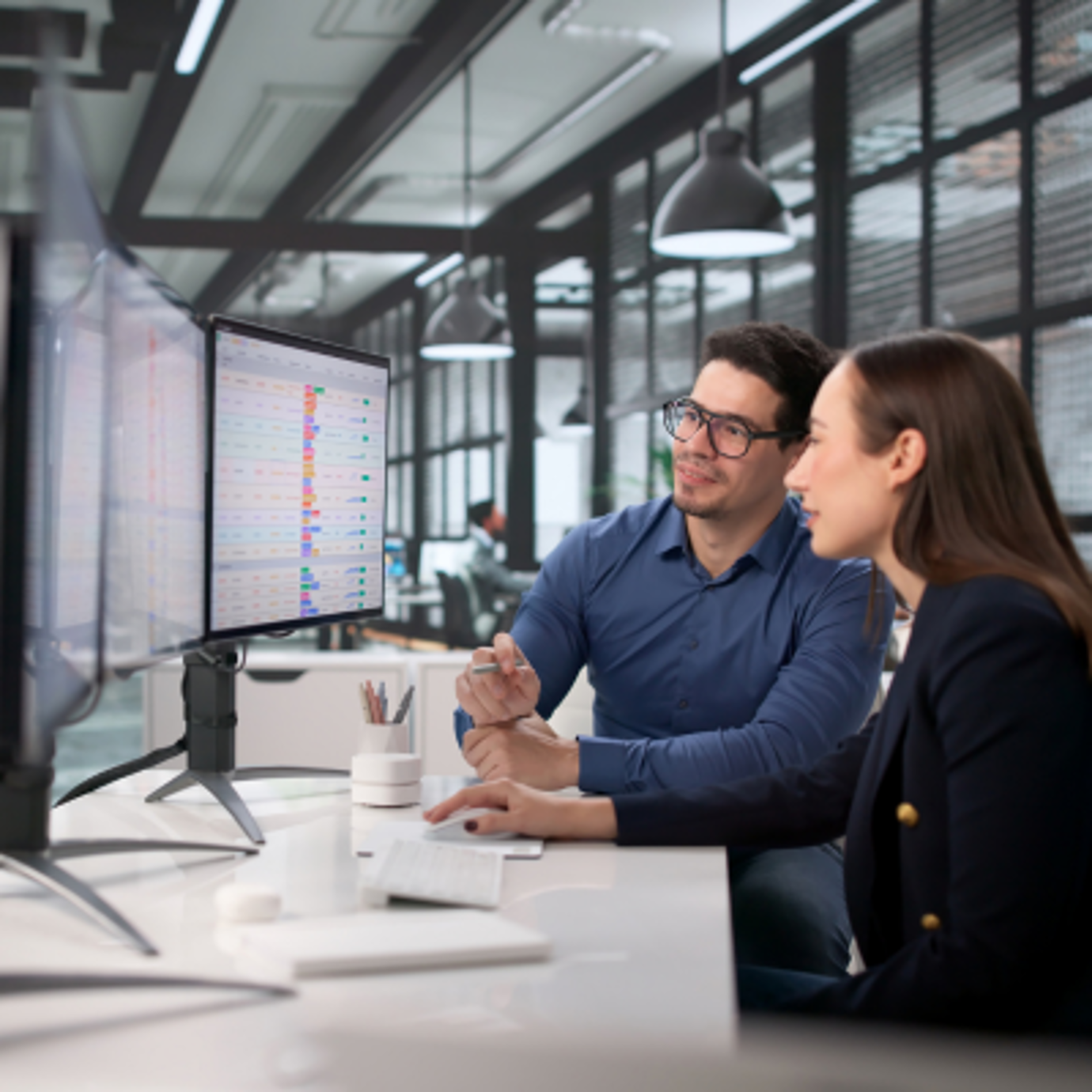 A man and a woman sat in an office looking at the same computer screens having a disucssion