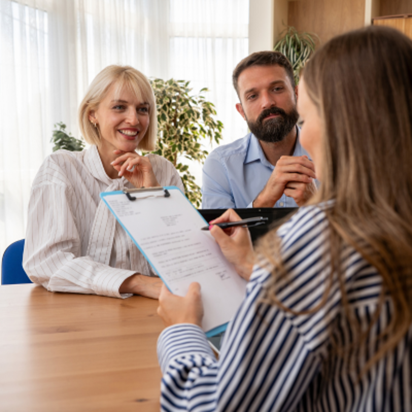 Smiling woman and a man reviewing documents with a female adviser during a consultation.