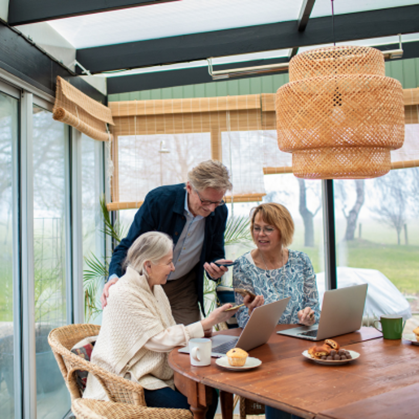 Three senior adults looking at a tablet together in a bright conservatory