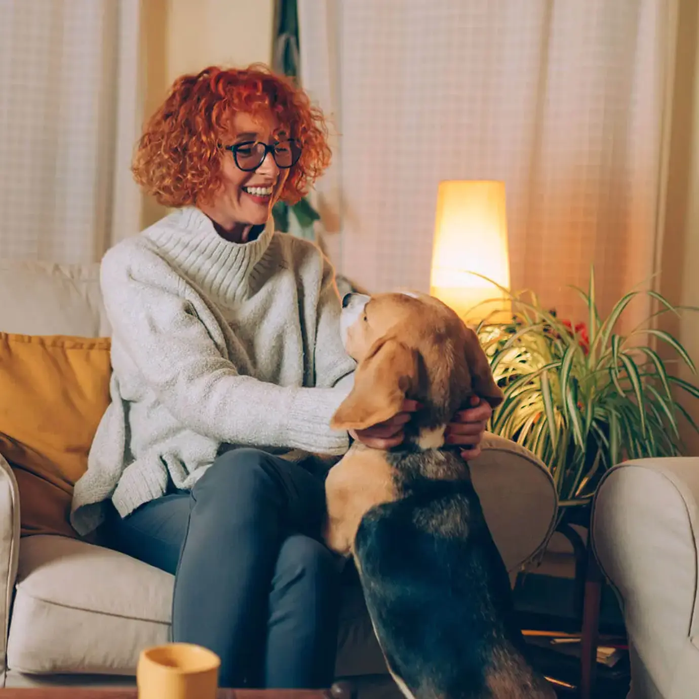 Smiling senior woman relaxing on a sofa at home while stroking her dog.