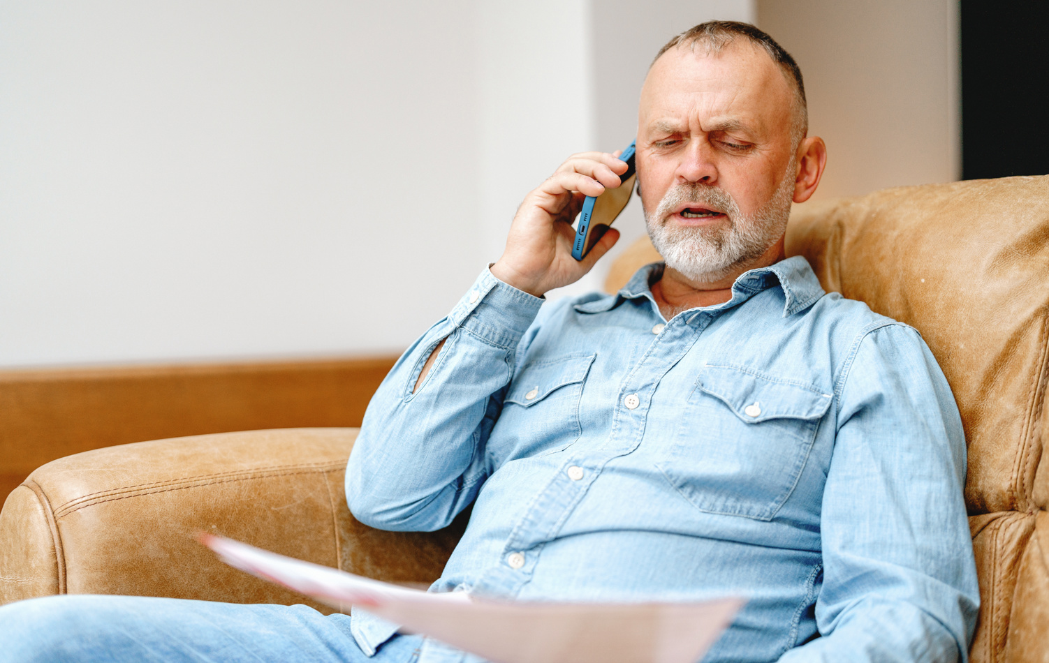 A man on the sofa holding a form while talking on the phone